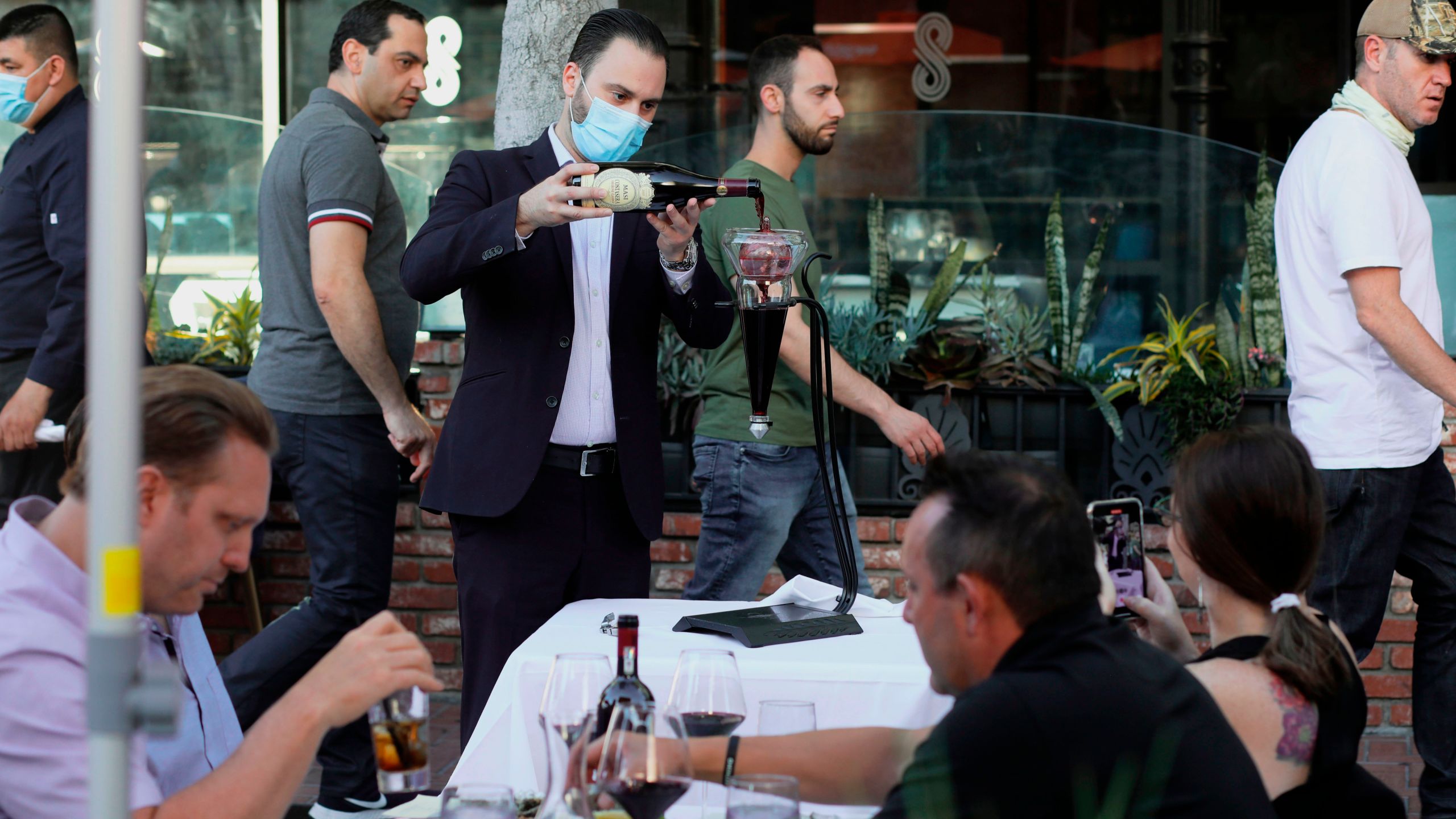 A waiter pours wine for patrons at an outdoor restaurant along 5th Avenue in The Gaslamp Quarter in downtown San Diego, California on July 17, 2020. (SANDY HUFFAKER/AFP via Getty Images)