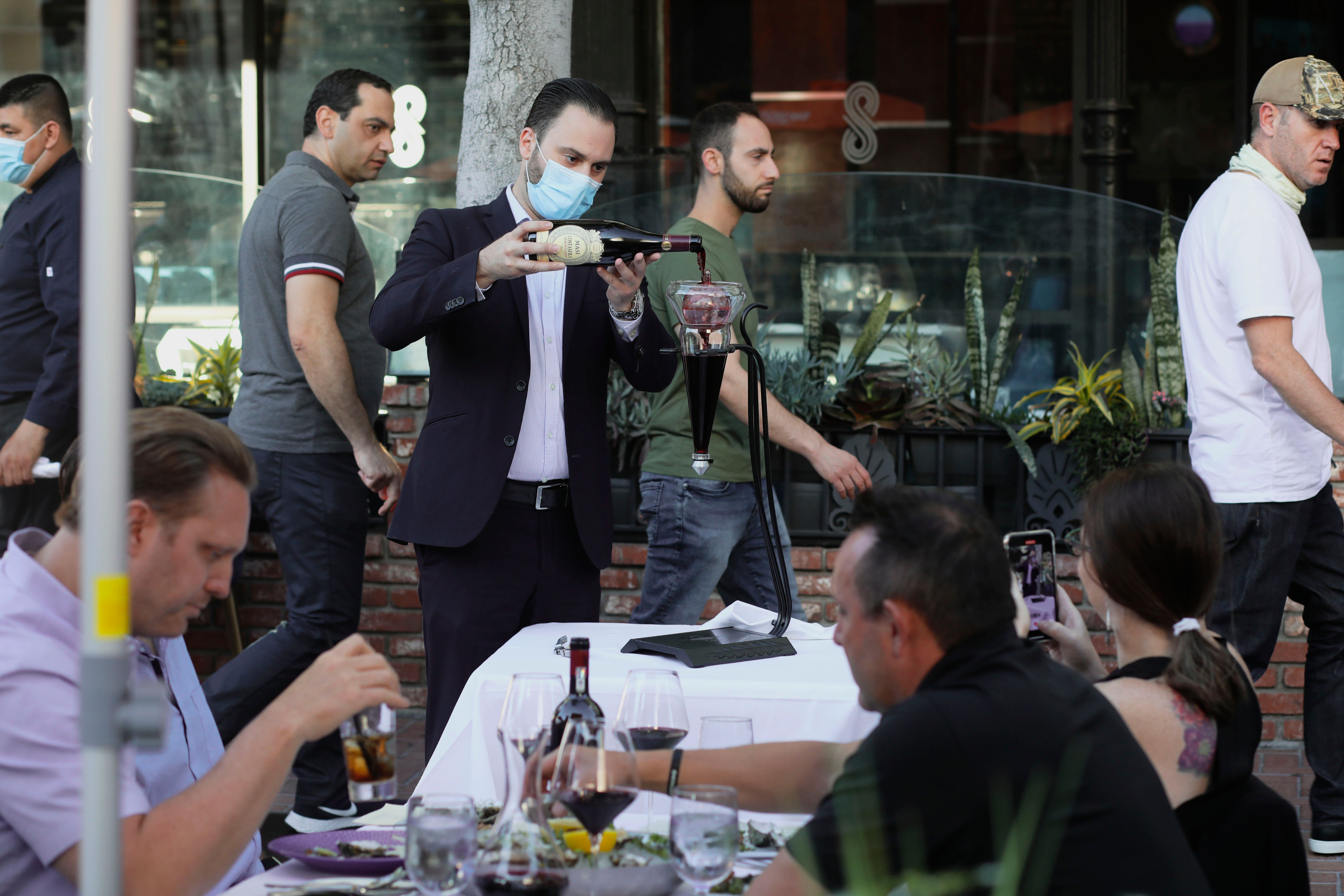 A waiter pours wine for patrons at an outdoor restaurant along 5th Avenue in The Gaslamp Quarter in downtown San Diego, California on July 17, 2020. (SANDY HUFFAKER/AFP via Getty Images)