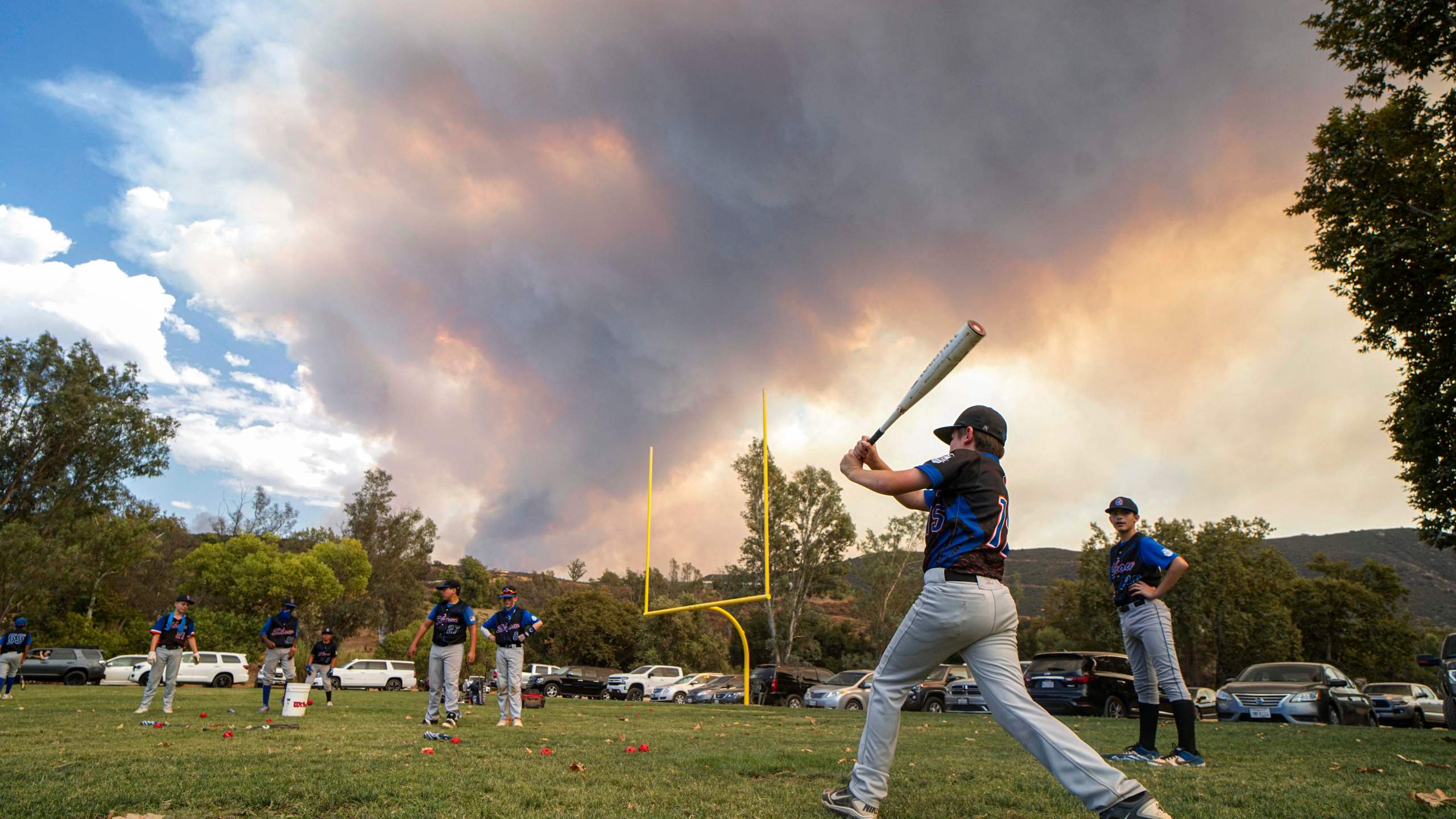 Little League players warm-up before a game as a brush fire is ablaze in back at a field next to the Sycuan Casino on the Sycuan Indian reservation during the Valley Fire, near Dehesa, in San Diego, California on Sept. 6, 2020. (SANDY HUFFAKER/AFP via Getty Images)