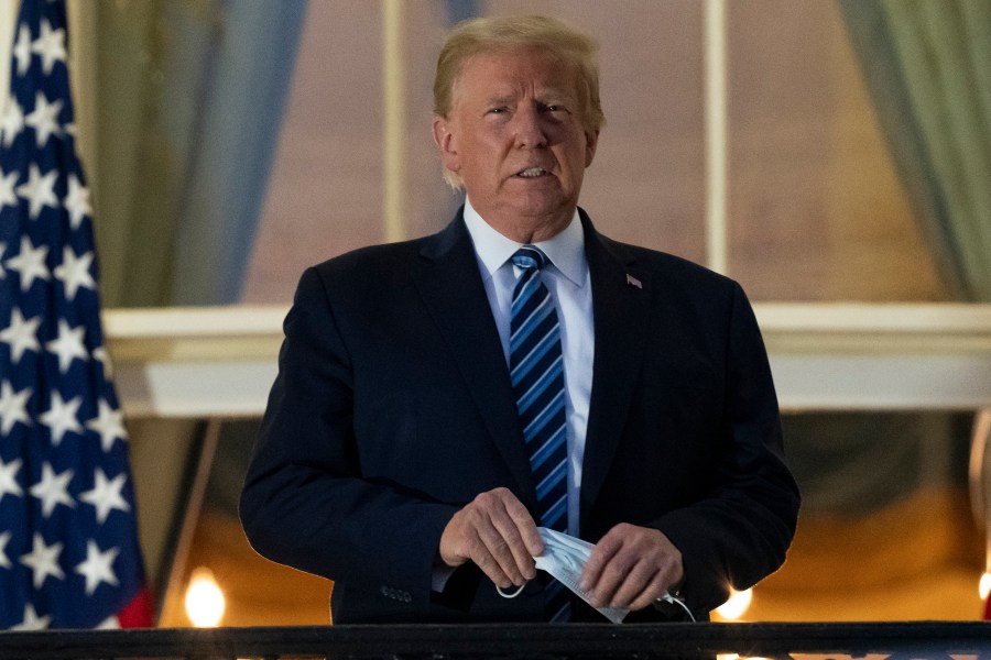 President Donald Trump holds his mask after removing it from his face as he stands on the Blue Room Balcony upon returning to the White House from the Walter Reed military hospital on Oct. 5, 2020. (Alex Brandon / Associated Press)