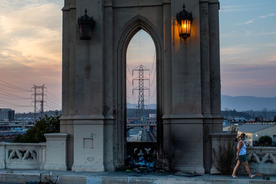 A woman wearing a face mask walks on the Fourth Street Bridge in Los Angeles with high tension towers in the background on Aug. 16, 2020, two days after California on Aug. 14 ordered rolling power outages for the first time since 2001. (Apu Gomes / AFP / Getty Images)