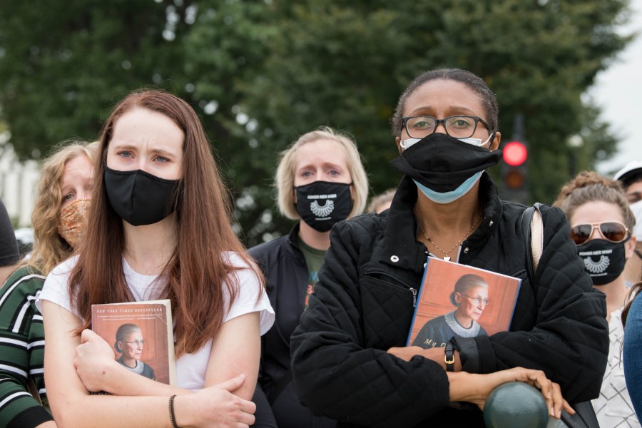 Women hold Justice Ruth Bader Ginsburg's book as they watch as her casket is carried down the steps of the U.S. Capitol on Sept. 25, 2020. (Liz Lynch / Getty Images)