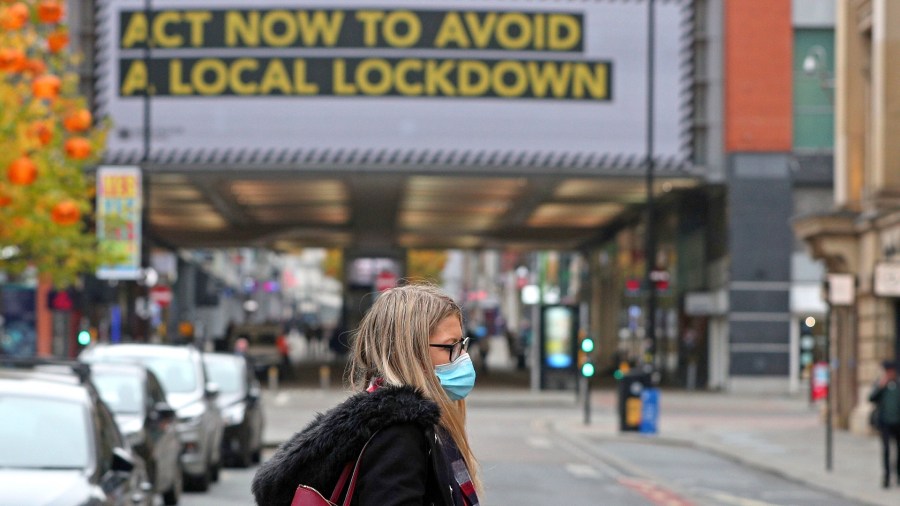 A woman wearing a face mask walks in Manchester, England, Monday, Oct. 19, 2020. (Peter Byrne/PA via AP)