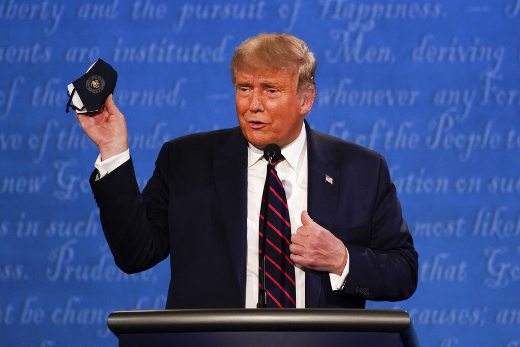 President Trump holds up his face mask during the first presidential debate at Case Western University and Cleveland Clinic, in Cleveland, Ohio. President Trump and first lady Melania Trump have tested positive for the coronavirus, the president tweeted early Friday. (AP Photo/Julio Cortez, File)