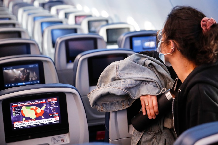 A passenger wears personal protective equipment on a Delta Airlines flight as a map depicting the spread of COVID-19 is displayed on a monitor after landing at Minneapolis−Saint Paul International Airport, Thursday, May 28, 2020, in Minneapolis. (AP Photo/John Minchillo)