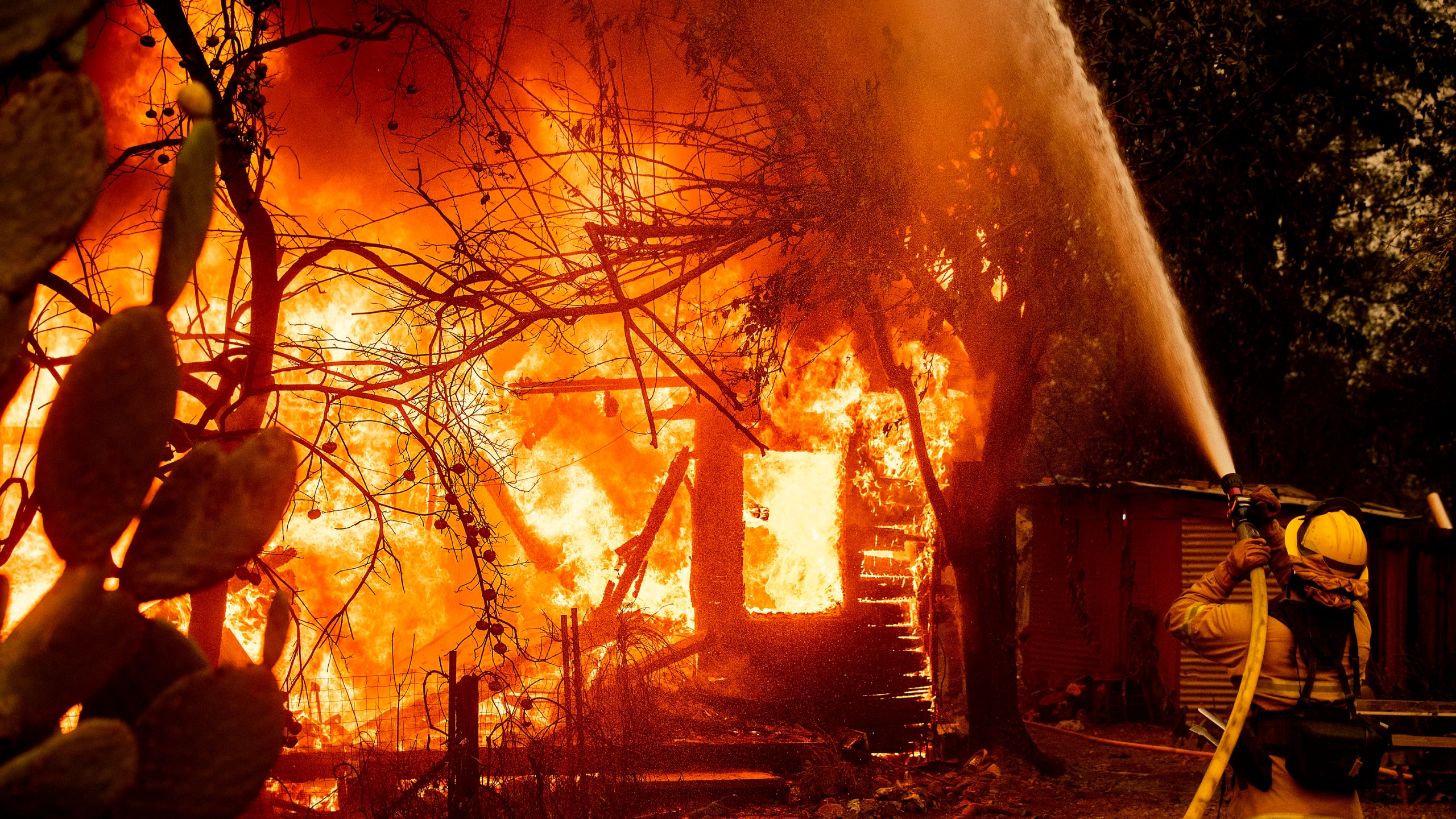 In this Oct. 24, 2019, file photo, a firefighter sprays water on a burning home as the Kincade Fire burns through the Jimtown community of unincorporated Sonoma County, Calif. Fire officials say Pacific Gas & Electric transmission lines sparked a wildfire last year in Northern California that destroyed hundreds of homes and led to the evacuation of nearly 100,000 people. The California Department of Forestry and Fire Protection issued the finding Thursday, July 16, 2020. (AP Photo/Noah Berger, File)