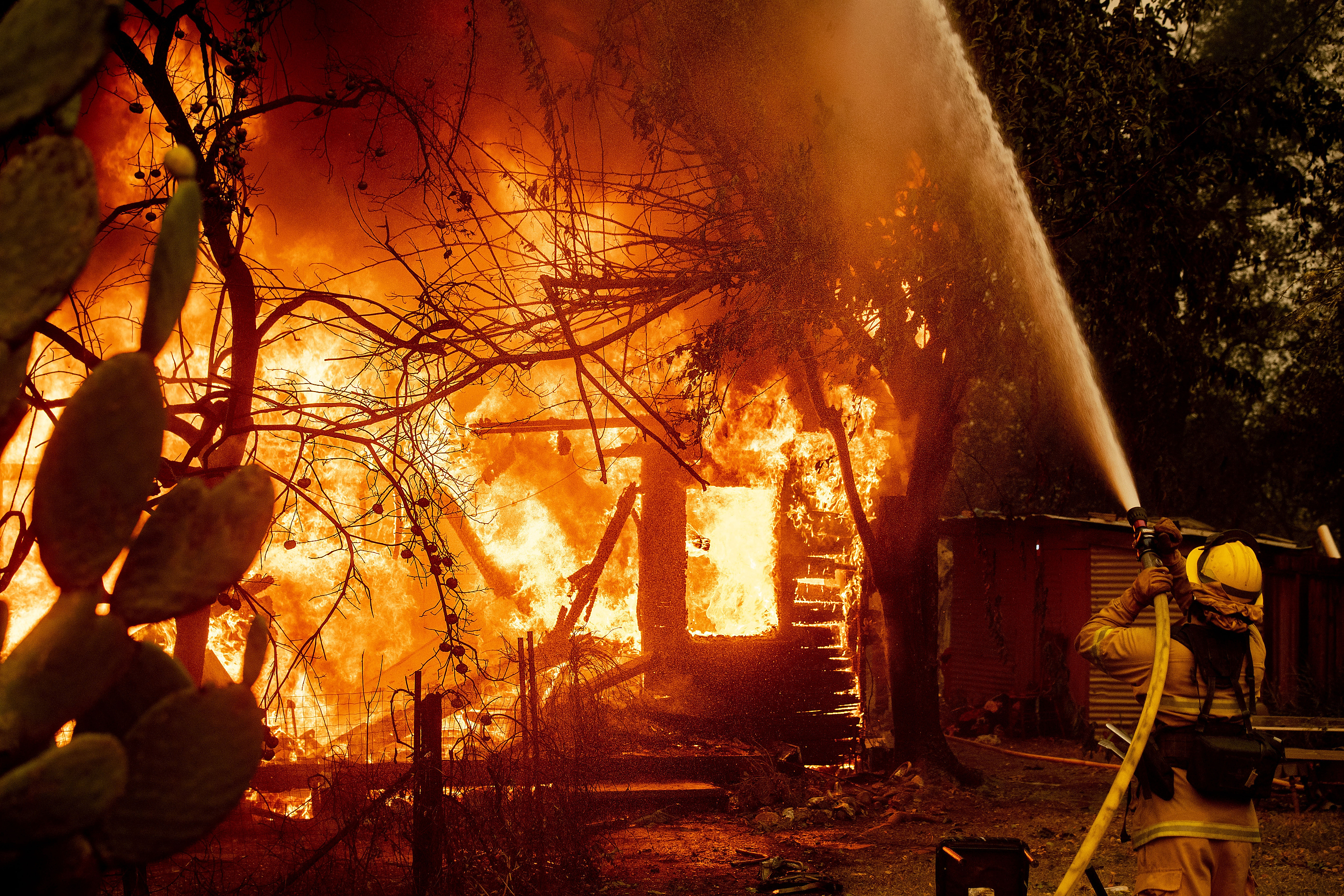 In this Oct. 24, 2019, file photo, a firefighter sprays water on a burning home as the Kincade Fire burns through the Jimtown community of unincorporated Sonoma County, Calif. Fire officials say Pacific Gas & Electric transmission lines sparked a wildfire last year in Northern California that destroyed hundreds of homes and led to the evacuation of nearly 100,000 people. The California Department of Forestry and Fire Protection issued the finding Thursday, July 16, 2020. (AP Photo/Noah Berger, File)