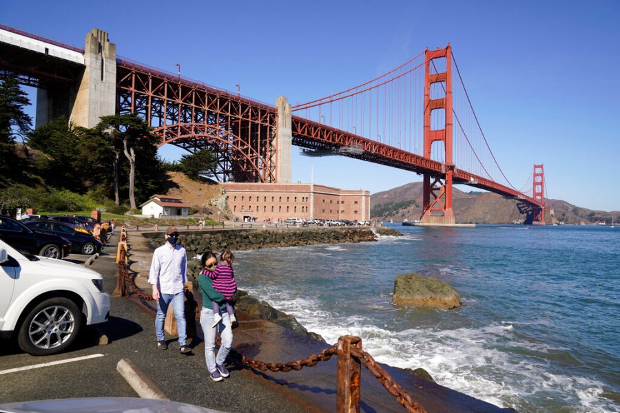 People walk along a seawall with Fort Point and the Golden Gate Bridge in the background in San Francisco on Oct. 11, 2020. (AP Photo/Eric Risberg)