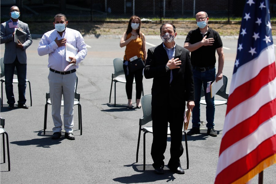 In this June 4, 2020, file photo, new citizens, socially distanced, recite the pledge of allegiance outside the U.S. Citizenship and Immigration Services building in Lawrence, Mass. (AP Photo/Elise Amendola, File)