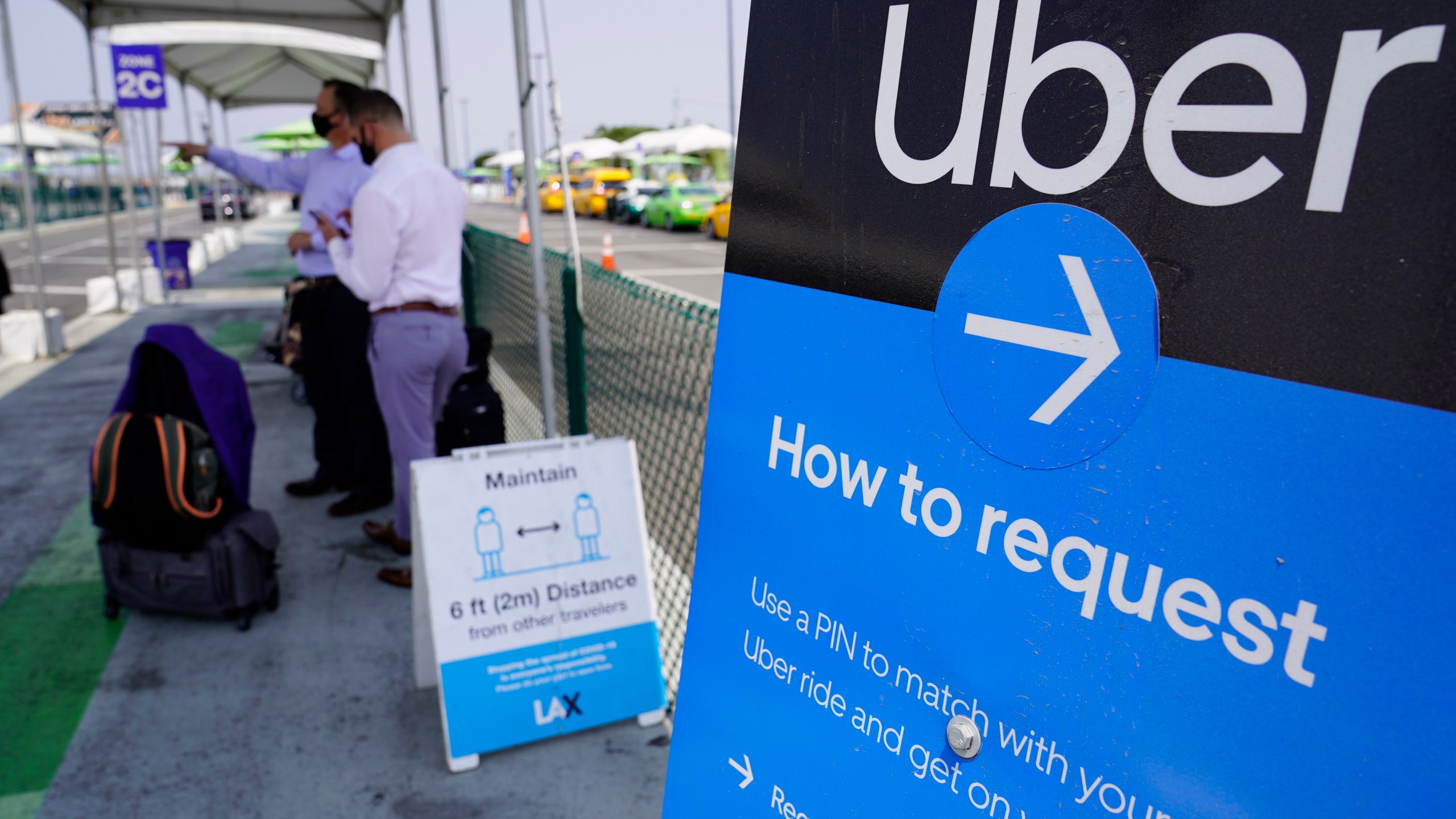 In this Aug. 20, 2020, file photo travelers request an Uber ride at Los Angeles International Airport's LAX-it pick up terminal. Uber, Lyft and other app-based ride-hailing and delivery services prevailed at the ballot box in their expensive gamble to keep drivers classified as independent contractors. Proposition 22 pitted the powerhouses of the so-called gig economy, including DoorDash, Postmates and Instacart, against labor unions. The measure creates an exemption to a state law that would have made drivers eligible for benefits that come with being company employees. (AP Photo/Damian Dovarganes, File)