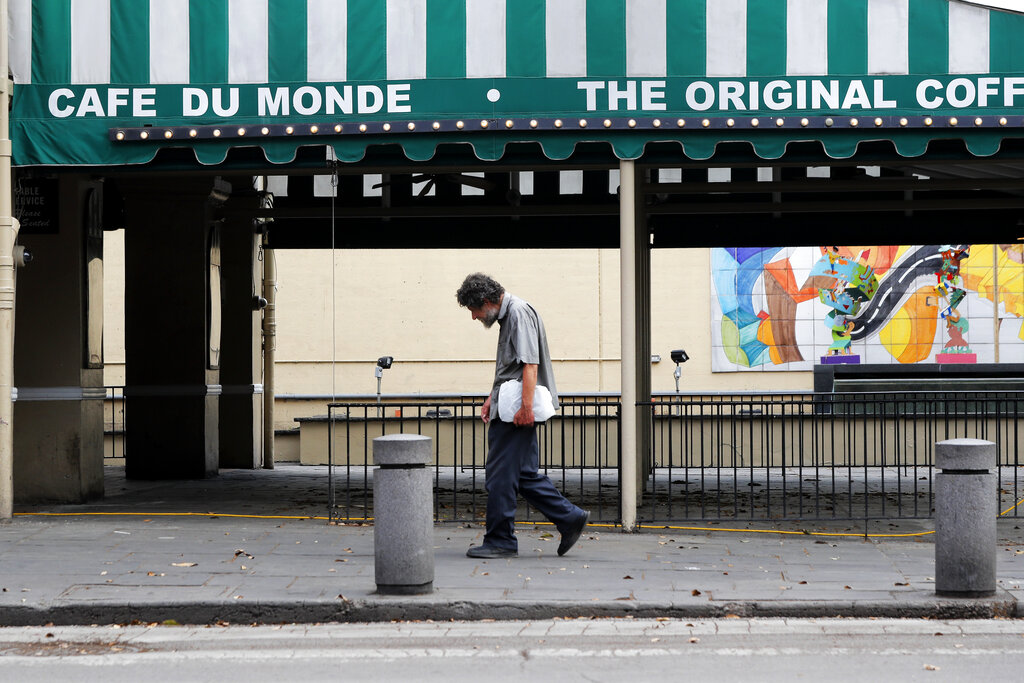 In this March 27, 2020, file photo, a man walks past the Cafe Du Monde restaurant, which was closed but has since reopened, in the French Quarter of New Orleans. (AP Photo/Gerald Herbert, File)