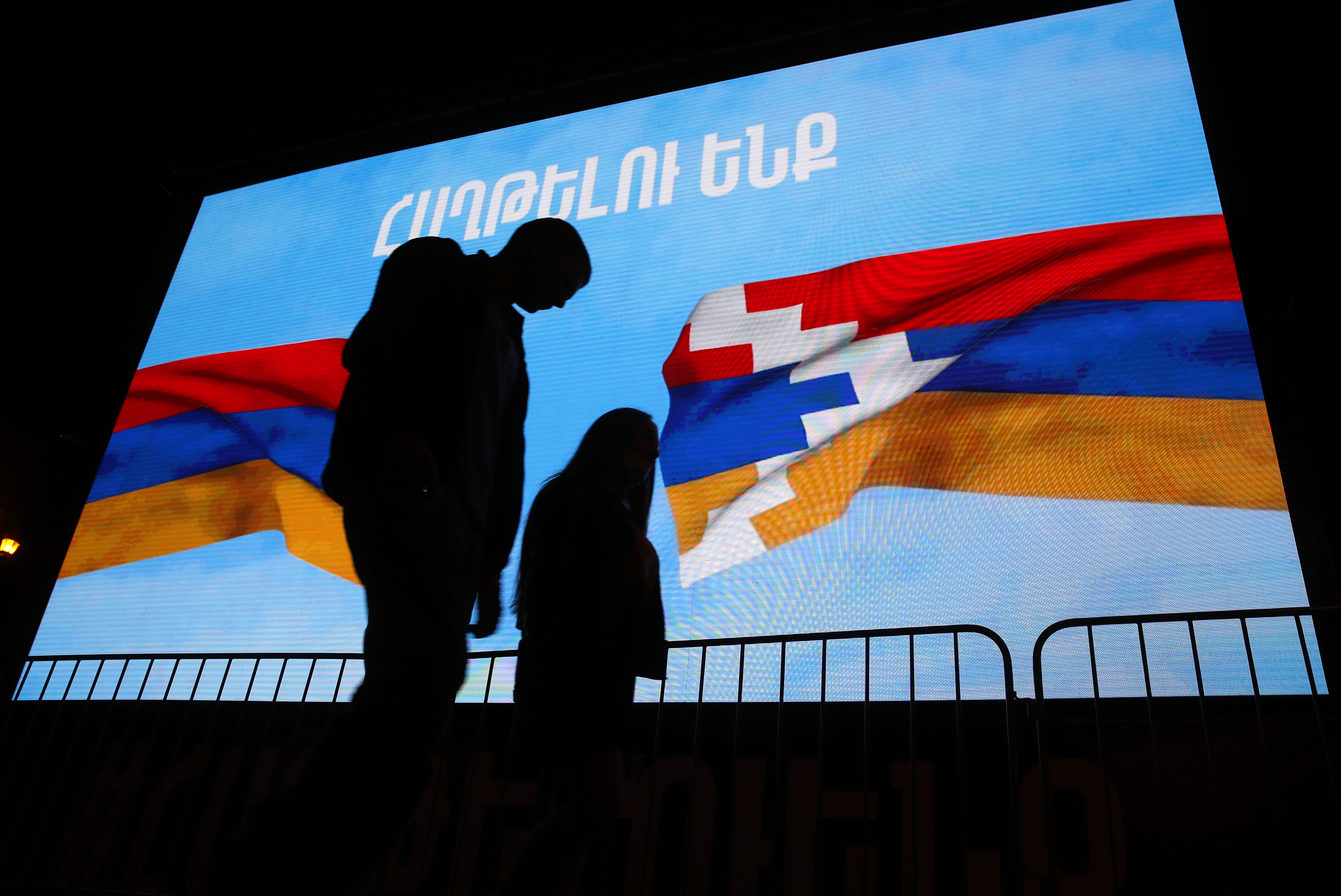 A couple walk past a screen displayed Armenian, left, and Nagorno-Karabakh's flags with sign reading "We will win" in Yerevan, the capital of Armenia on Nov. 9, 2020. (Associated Press)