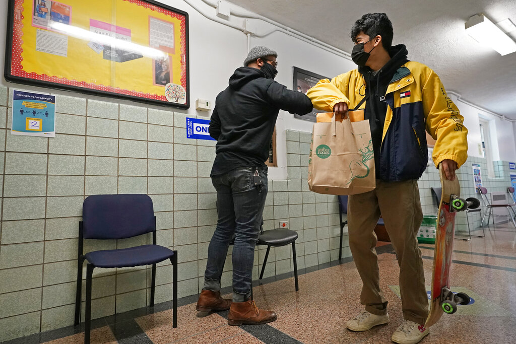 West Brooklyn Community High School principal Malik Lewis, left, bumps elbows with former student Jason Cardoso after Cardoso came to pick up the diploma he earned when he graduated in March, Thursday, Nov. 19, 2020, in the Brooklyn borough of New York. (AP Photo/Kathy Willens)