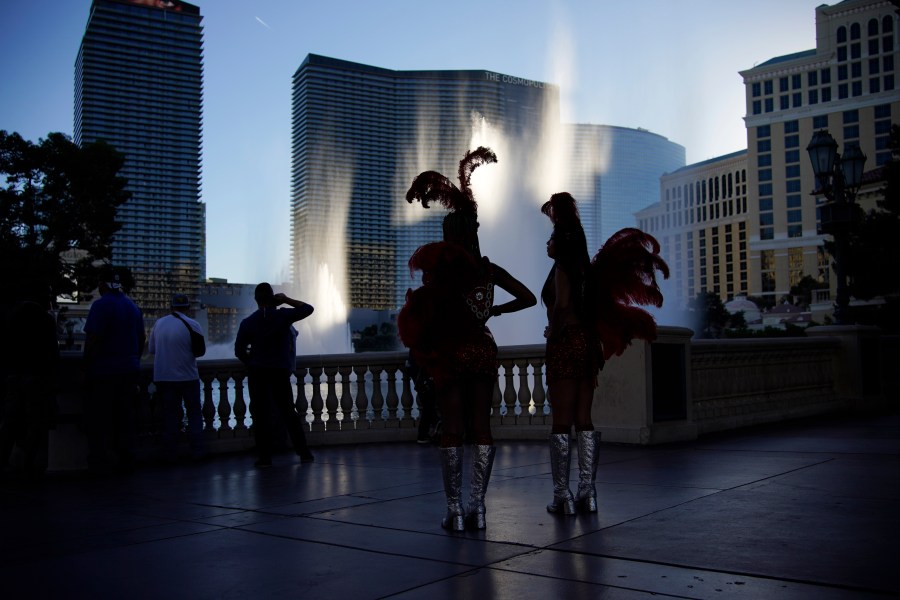 People dressed as showgirls stand along the Las Vegas Strip, Thursday, Nov. 19, 2020, in Las Vegas. As the coronavirus surges to record levels in Nevada, the governor has implored residents to stay home. But Democrat Steve Sisolak has also encouraged out-of-state visitors, the lifeblood of Nevada's limping economy, to come to his state and spend money in Las Vegas. (AP Photo/John Locher)