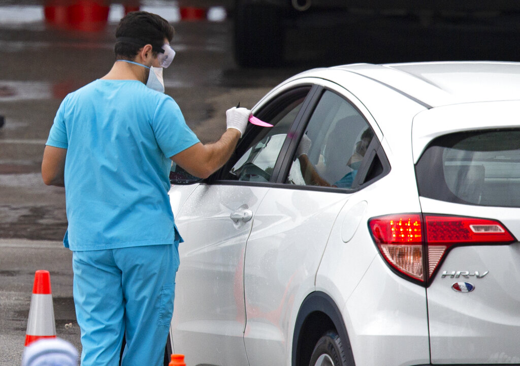 Vehicles line up as a healthcare worker helps to check in as citizens is being tested at the COVID-19 drive-thru testing center at Hard Rock Stadium in Miami Gardens on Sunday, November 22, 2020. (David Santiago/Miami Herald via AP)