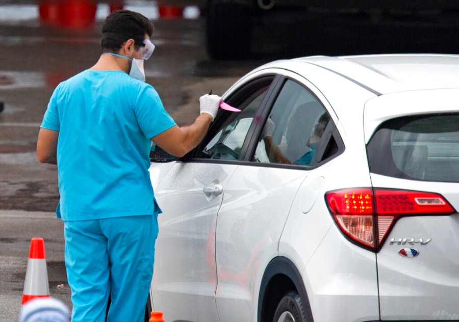 Vehicles line up as a healthcare worker helps to check in as citizens is being tested at the COVID-19 drive-thru testing center at Hard Rock Stadium in Miami Gardens on Sunday, November 22, 2020. (David Santiago/Miami Herald via AP)