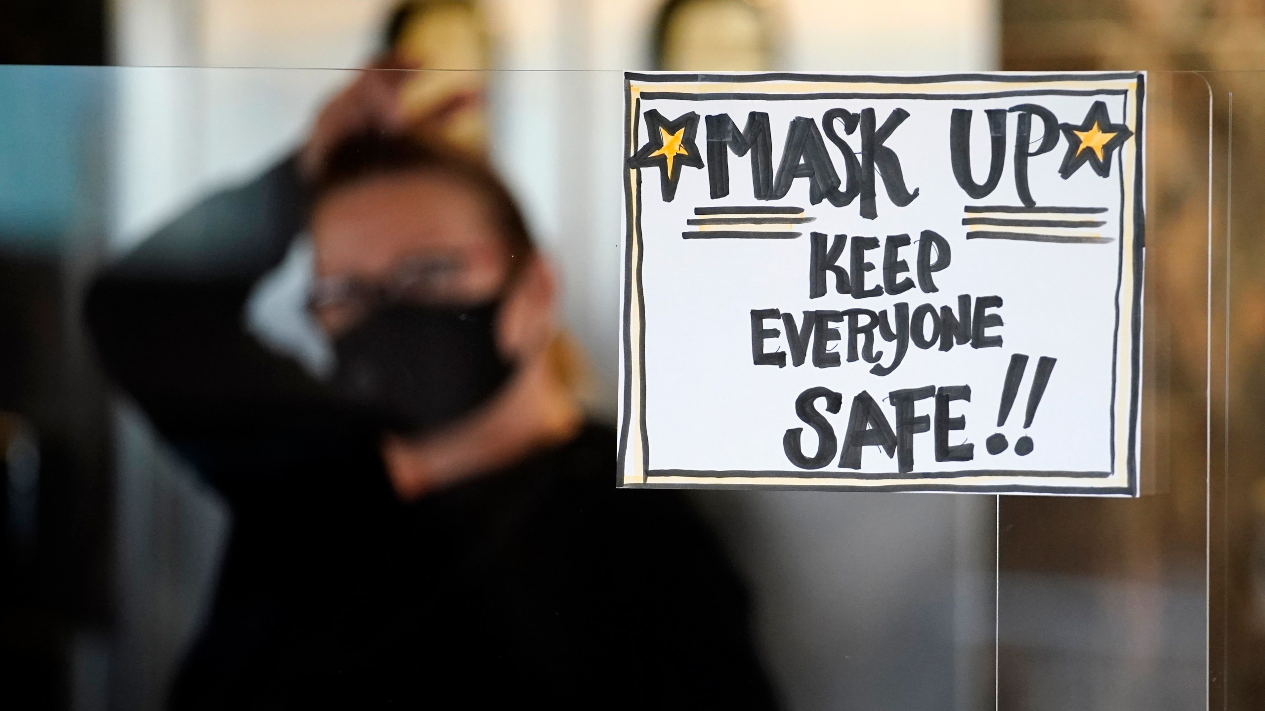 In this Tuesday, Nov. 17, 2020 file photo, manager Yllka Murati waits for a delivery driver to pick up takeout orders behind a partition displaying a sign to remind customers to wear a mask, at the Penrose Diner, in south Philadelphia. (AP Photo/Matt Slocum, File)