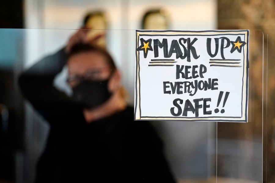 In this Tuesday, Nov. 17, 2020 file photo, manager Yllka Murati waits for a delivery driver to pick up takeout orders behind a partition displaying a sign to remind customers to wear a mask, at the Penrose Diner, in south Philadelphia. (AP Photo/Matt Slocum, File)