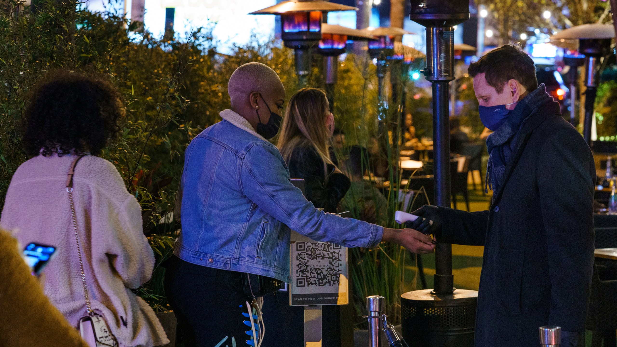 A staff member checks the temperature of an arriving diner at Katana Japanese restaurant in West Hollywood, Calif., Tuesday, Nov. 24, 2020. (AP Photo/Damian Dovarganes)