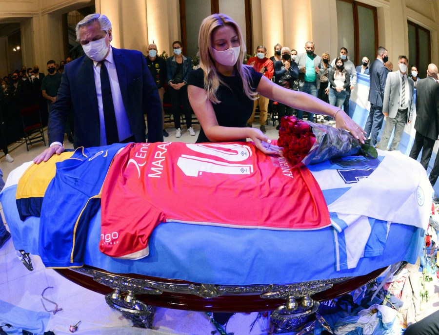 In this handout photo released by Argentina's Presidency, President Alberto Fernandez touches the coffin that contain the remains of Diego Maradona, while first lady Fabiola Yañez places a bouquet of roses on the casket adorned with his team jerseys, as they pay their final respects to Maradona, inside the presidential palace in Buenos Aires on Nov. 26, 2020. (Argentina's Presidency via Associated Press)