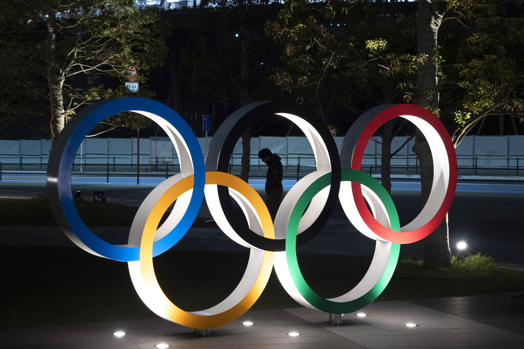 In this March 24, 2020, file photo, a man is seen through the Olympic rings in front of the New National Stadium in Tokyo.