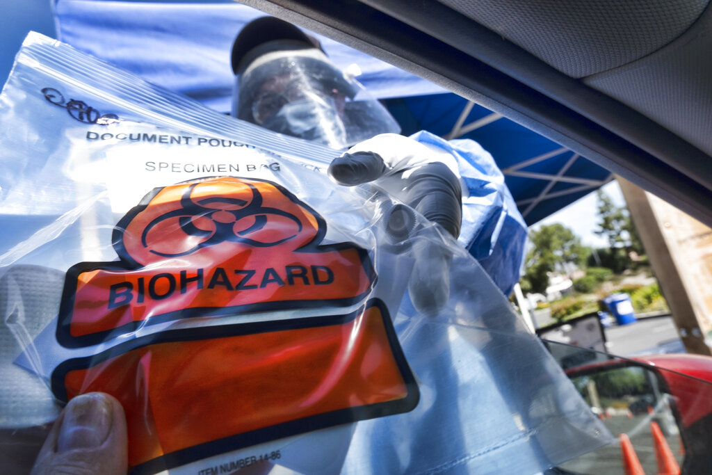 In this May 6, 2020 file photo a medical worker hands a self administered coronavirus test to a patient at a drive through testing site in a parking lot in the Woodland Hills. (AP Photo/Richard Vogel, File)