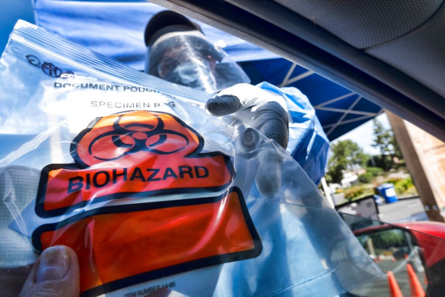 In this May 6, 2020 file photo a medical worker hands a self administered coronavirus test to a patient at a drive through testing site in a parking lot in the Woodland Hills. (AP Photo/Richard Vogel, File)