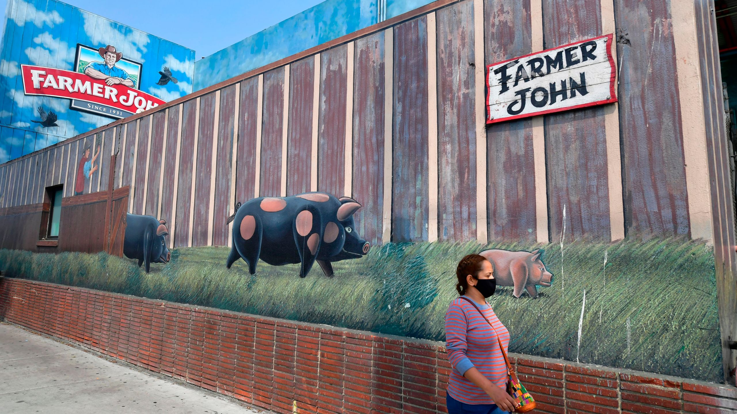 In this Sept. 14, 2020, photo, a woman wears a facemask while walking past the Farmer John plant in Vernon, which was hit with a safety fine after an outbreak of hundreds of coronavirus cases. (Frederic J. Brown / AFP / Getty Images)