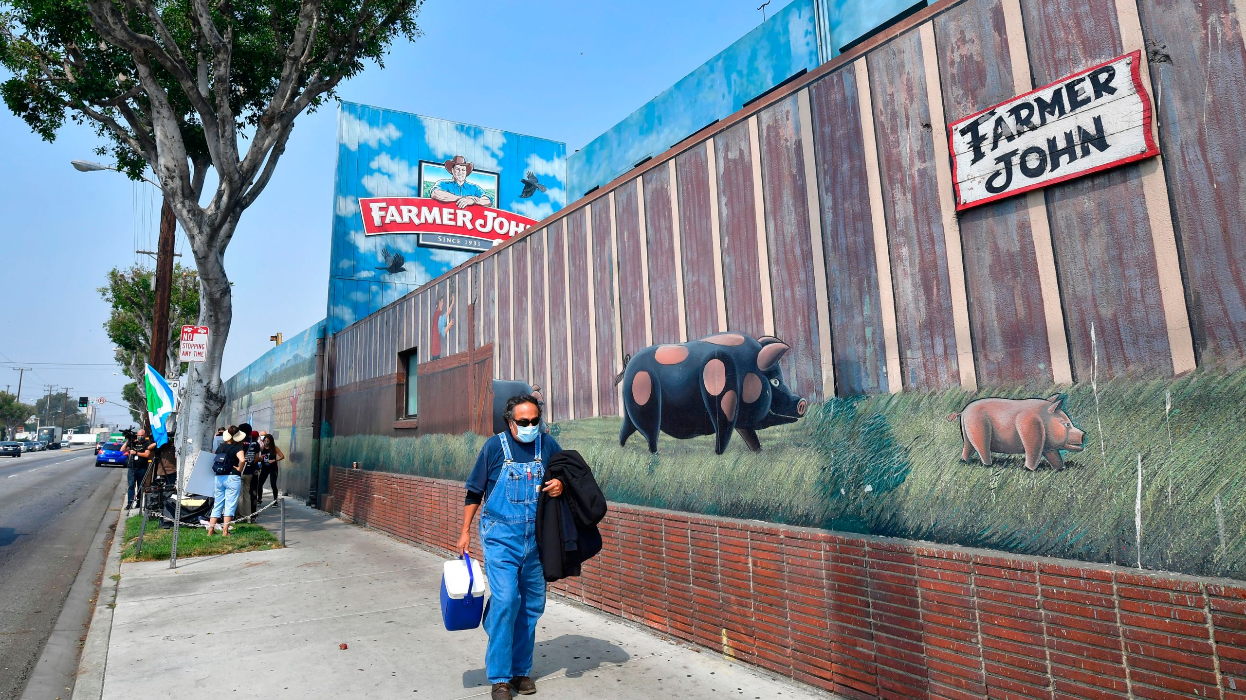 A worker finishing his shift carries a cooler past activists from groups such as LA Animal Save, Slaughter Free Los Angeles and Direct Action Everywhere gathered to demonstrate outside the Farmer John Slaughterhouse/Packing plant in Vernon, an industrial city five miles south of downtown Los Angeles on September 14, 2020 (Frederic J. Brown/AFP via Getty Images)