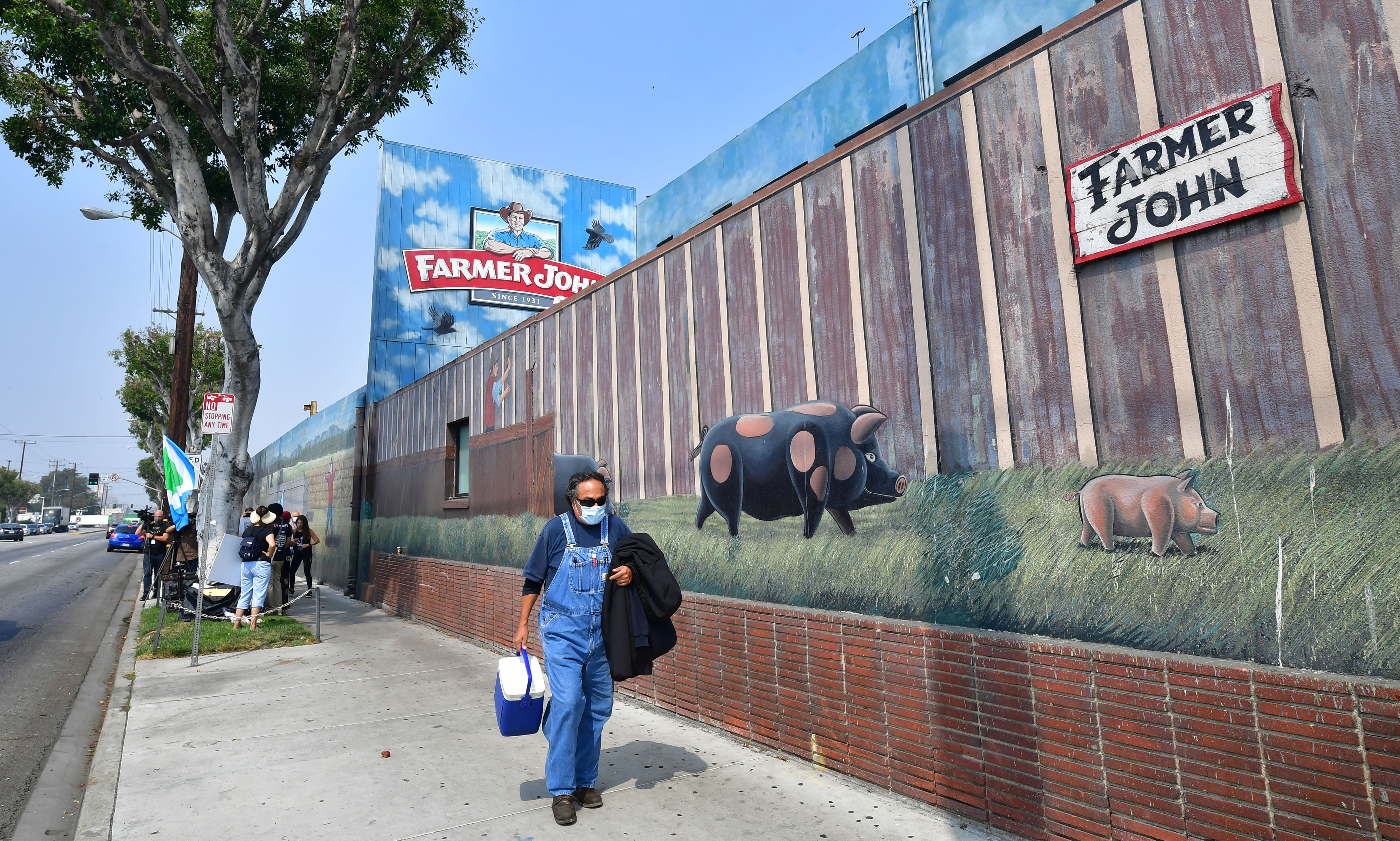 A worker finishing his shift carries a cooler past activists from groups such as LA Animal Save, Slaughter Free Los Angeles and Direct Action Everywhere gathered to demonstrate outside the Farmer John Slaughterhouse/Packing plant in Vernon, an industrial city five miles south of downtown Los Angeles on September 14, 2020 (Frederic J. Brown/AFP via Getty Images)