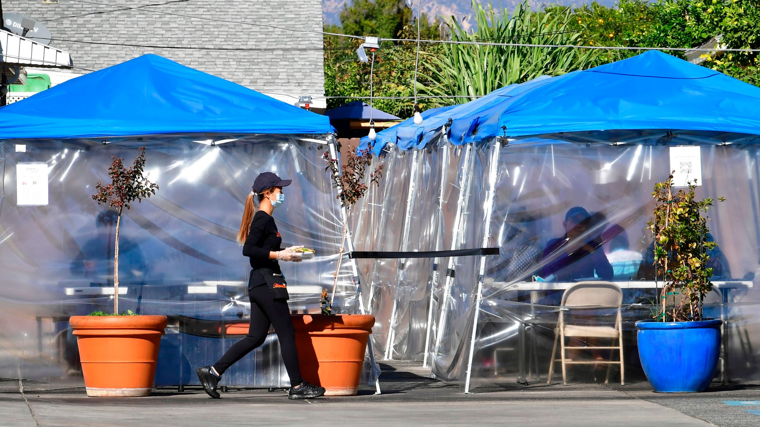 A waitress delivers orders to diners seated outdoors under tents in a restaurant's parking lot on Nov. 17, 2020 in Alhambra. (FREDERIC J. BROWN/AFP via Getty Images)