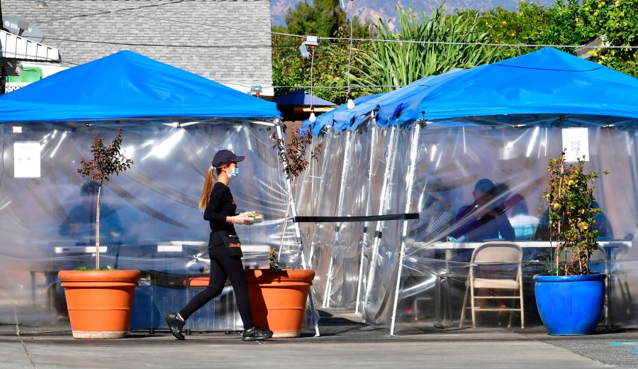 A waitress delivers orders to diners seated outdoors under tents in a restaurant's parking lot on Nov. 17, 2020 in Alhambra. (FREDERIC J. BROWN/AFP via Getty Images)