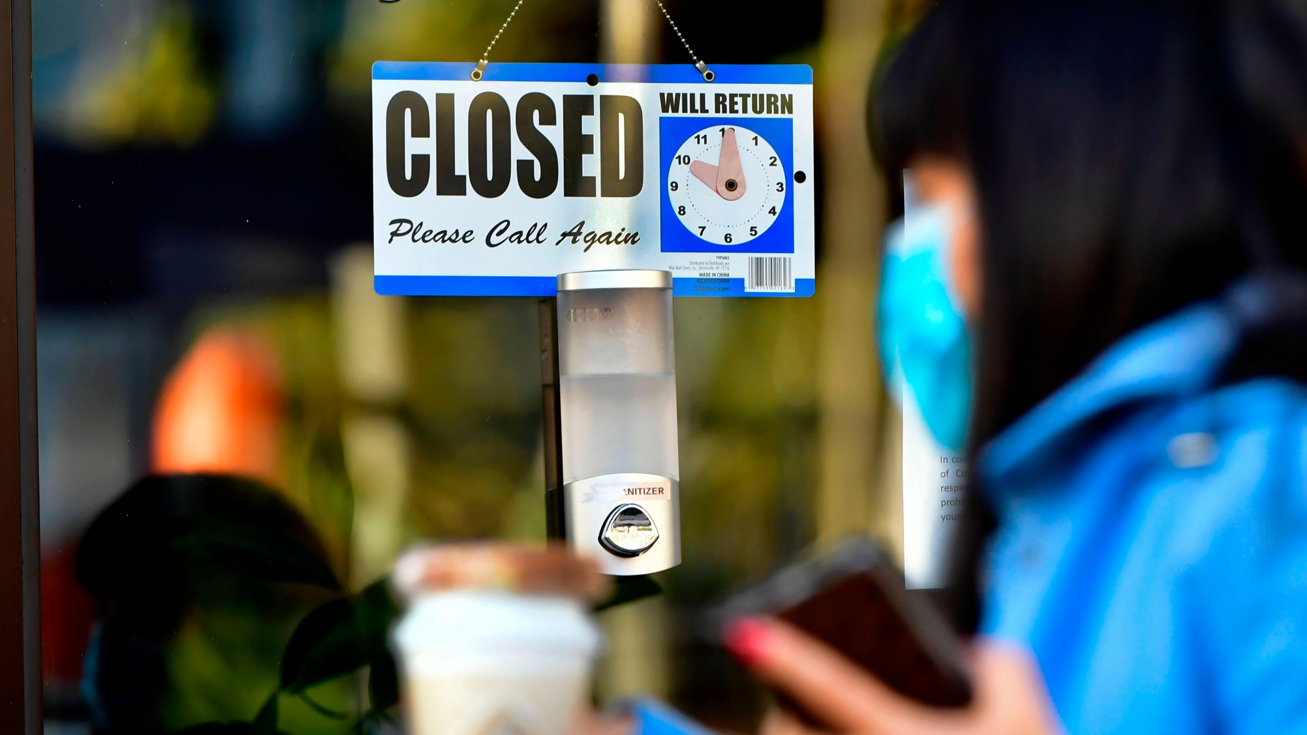 A pedestrian wearing her facemask and holding a cup of coffee walks past a closed sign hanging on the door of a small business in Los Angeles on Nov. 30, 2020. (Frederic J. Brown / AFP / Getty Images)