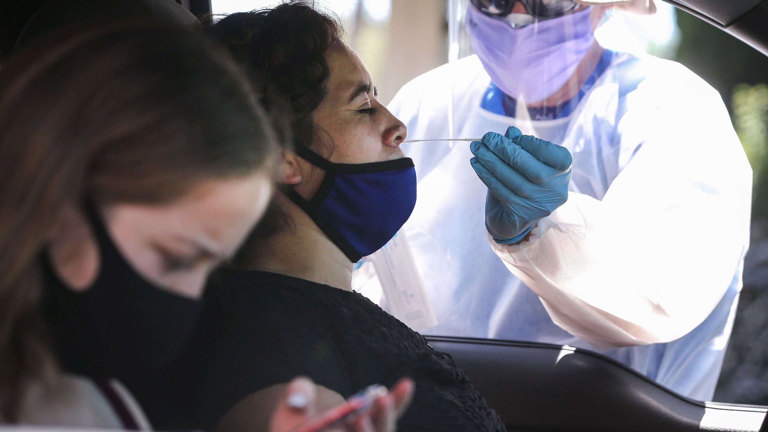 A healthcare worker assists a motorist with a nasal swab test at a drive-in coronavirus testing center on Aug.11, 2020 in Los Angeles. (Mario Tama/Getty Images)