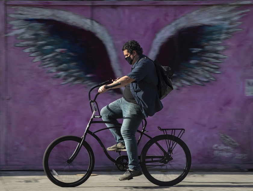 A bicyclist wearing a mask pedals on Melrose Avenue. If he stops and goes inside a store, he’ll need to keep the mask on.(Mel Melcon / Los Angeles Times)