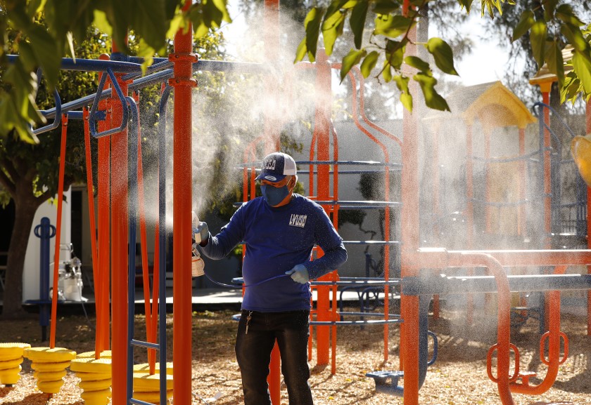 Custodian Carlo Ramos sprays a disinfecting solution on playground equipment at Lupin Hill Elementary School, one of the first L.A. County public schools to open under a special waiver. (Al Seib / Los Angeles Times)