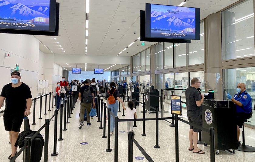 A TSA agent, masked and sitting behind an acrylic panel, checks an ID at Salt Lake City International Airport in an undated photo. (DANIEL SLIM/AFP via Getty Images)