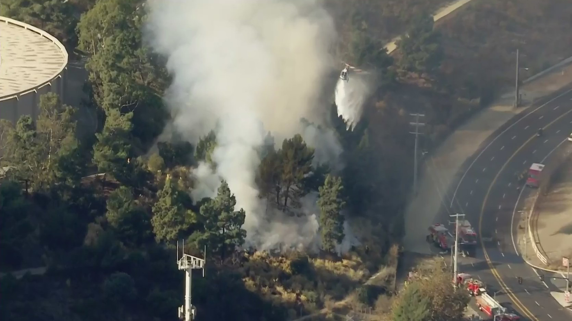 A helicopter makes a water drop on a blaze along the 405 Freeway in Bel-Air on Dec. 16, 2020. (KTLA)