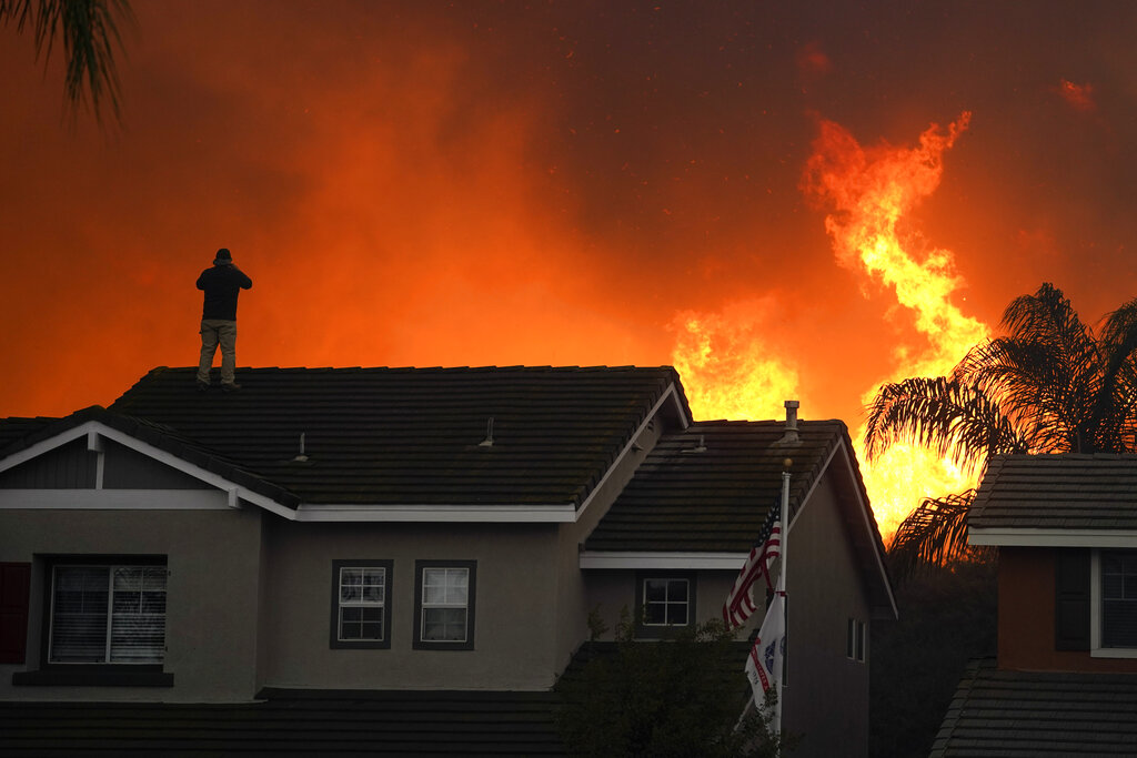 In this Tuesday, Oct. 27, 2020 file photo, Herman Termeer, 54, stands on the roof of his home as the Blue Ridge Fire burns along the hillside in Chino Hills, Calif. (AP Photo/Jae C. Hong)