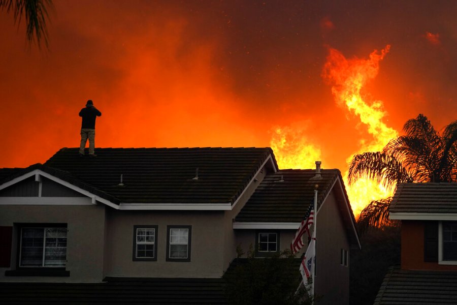 In this Tuesday, Oct. 27, 2020 file photo, Herman Termeer, 54, stands on the roof of his home as the Blue Ridge Fire burns along the hillside in Chino Hills, Calif. (AP Photo/Jae C. Hong)