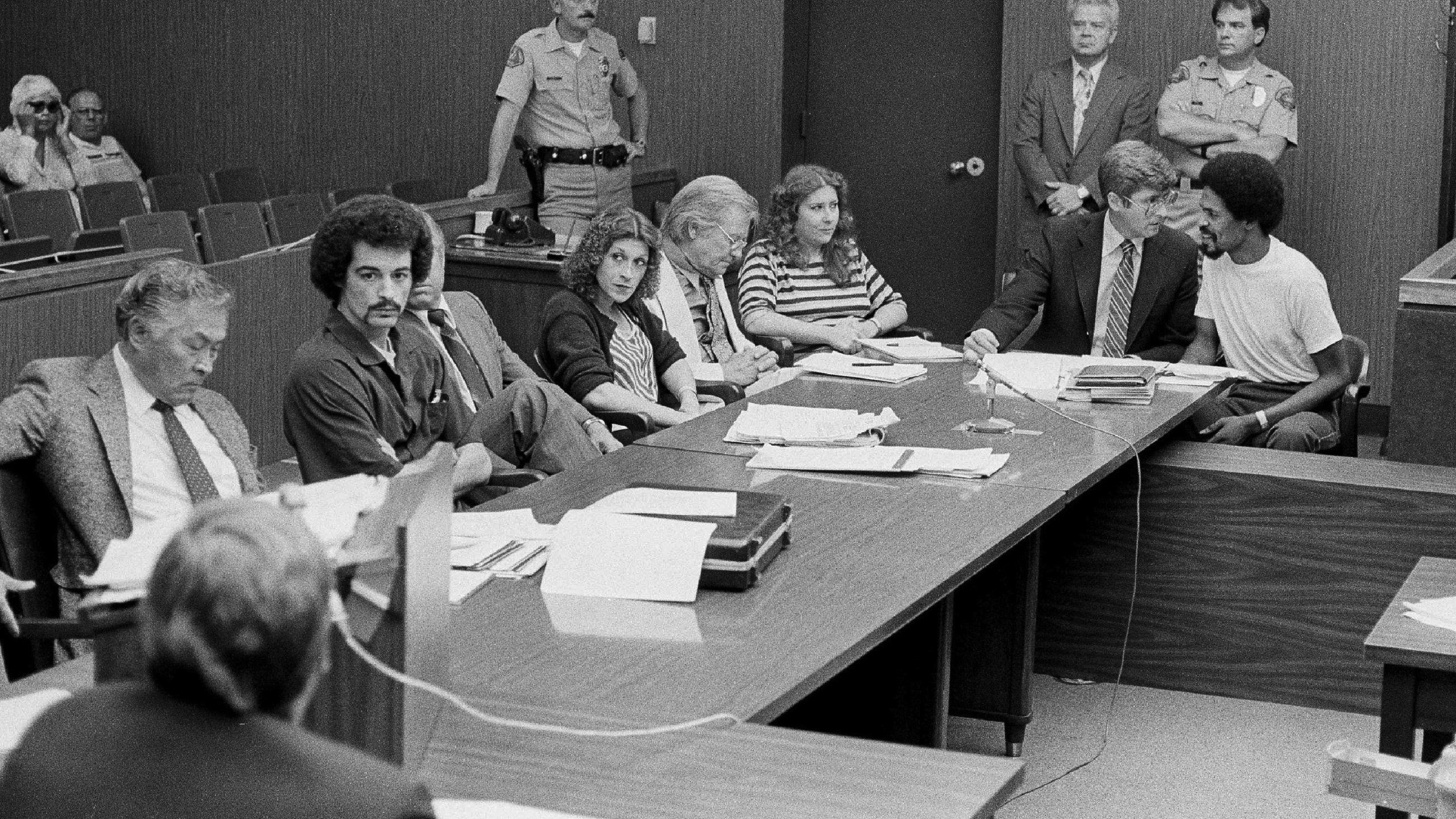 In this Aug. 22, 1983, file photo, four persons charged in connection with the June 2, 1983, fatal shooting of Los Angeles Police Officer Paul Verna sit with their attorneys during a preliminary hearing in a San Fernando, Calif., courtroom. Seated second from left to right, Kenneth Gay, an unidentified attorney, Robin Gay, attorney Elmer Docken, Pam Cummings, attorney Edward Rucker and Reynard Cummings. (AP Photo/Michael Tweed, File)