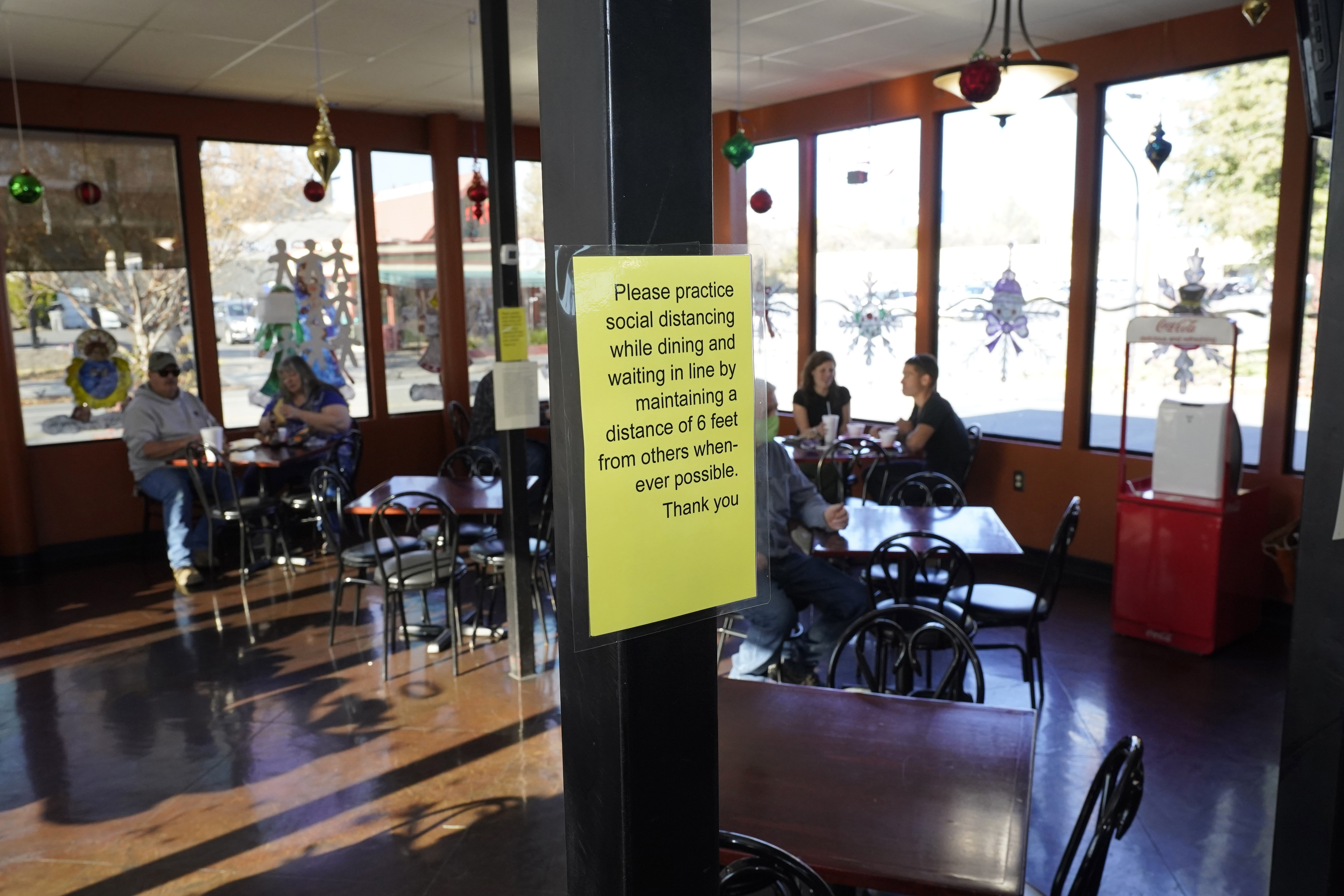 A sign advising patrons to maintain social distancing is posted in the indoor dining area of the San Francisco Deli in Redding, Calif., Thursday, Dec. 3, 2020. Brenda Luntey, who owns the deli with her husband, is openly violating the state's order to close her restaurant to indoor dining. She takes all the precautions advised, but doesn't force customers to wear a face mask. Luntey wants her customers and critics to know she is not a rule-breaker, and that it’s a matter of survival. (AP Photo/Rich Pedroncelli)