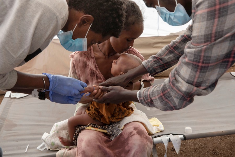 A Tigray woman who fled the conflict in Ethiopia's Tigray region, holds her malnourished and severely dehydrated baby as nurses give him IV fluids, at the Medecins Sans Frontieres (MSF) clinic, at Umm Rakouba refugee camp in Qadarif, eastern Sudan, Saturday, Dec. 5, 2020. (Nariman El-Mofty/AP Photo)