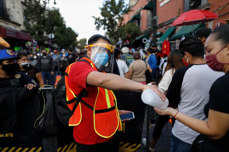 A city worker offers antibacterial gel to passing shoppers as they walk in a crowded commercial district of central Mexico City, Saturday, Dec. 5, 2020. (AP Photo/Rebecca Blackwell)