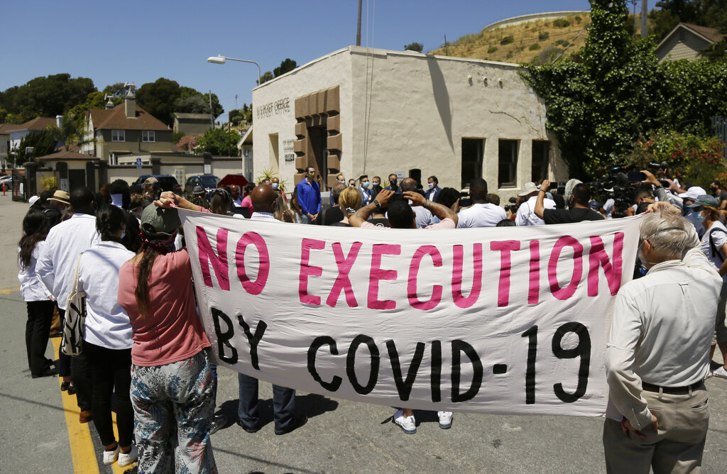 In this July 9, 2020, file photo, people hold up a banner while listening to a news conference outside San Quentin State Prison in San Quentin. (AP Photo/Eric Risberg, File)