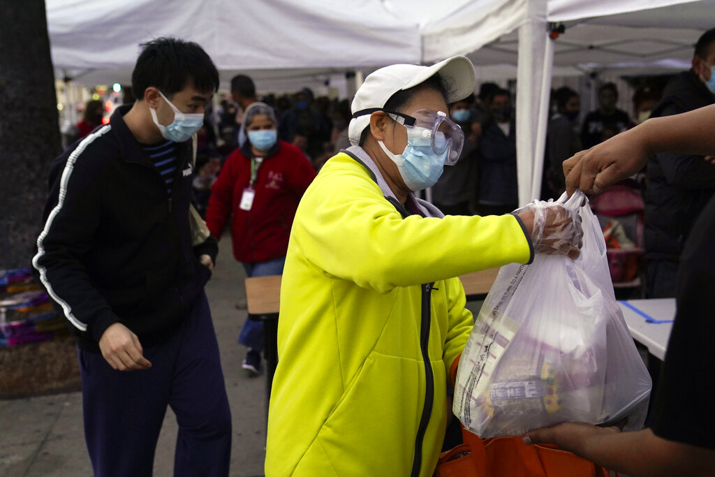 A woman receives a bag of groceries at a food bank at the Los Angeles Boys & Girls Club in the Lincoln Heights neighborhood of Los Angeles, Thursday, Dec. 17, 2020. (AP Photo/Jae C. Hong)