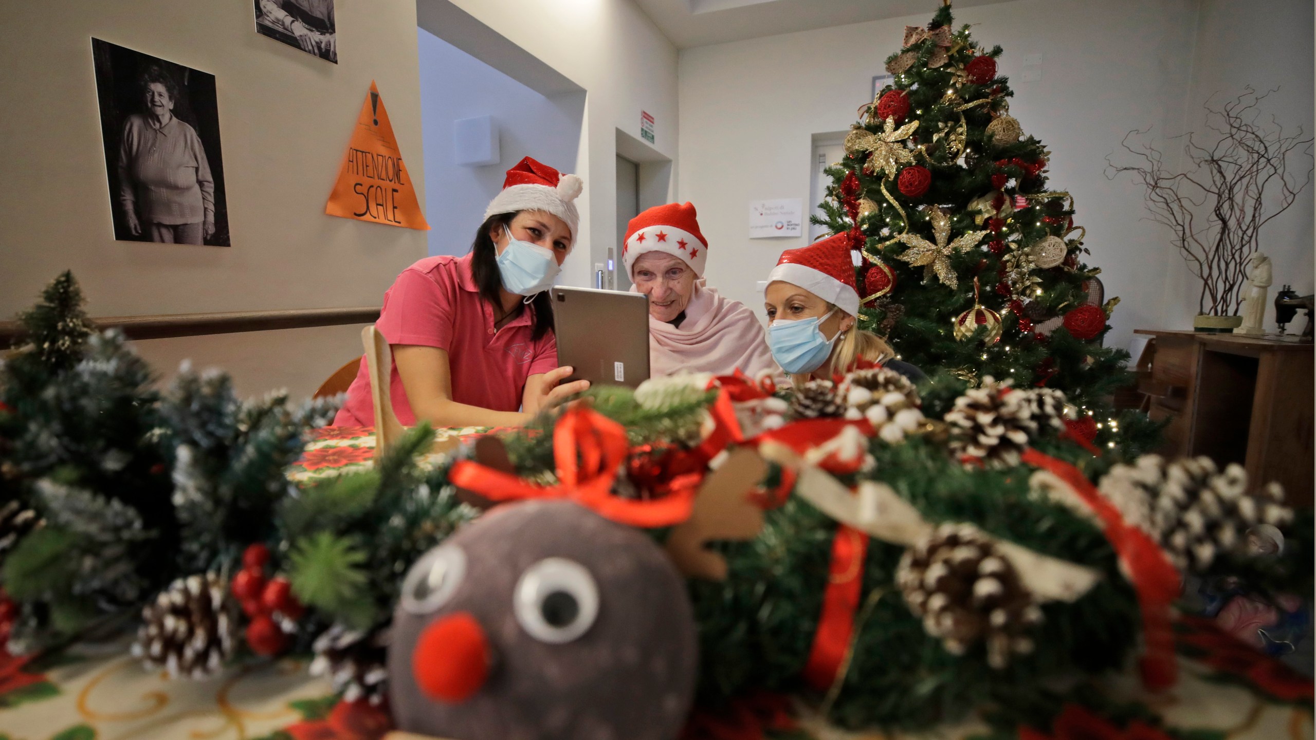 In this Dec. 19, 2020, file photo, Augusta Grigis, is flanked by nurse Michela Valle, left, and director Maria Giulia Madaschi, as she talks via a tablet with a donor who bought and sent her a Christmas present through an organization dubbed "Santa's Grandchildren", at a nursing home in Alzano Lombardo, in Northern Italy. (Luca Bruno/AP Photo)