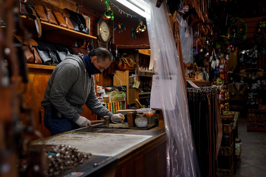 Leather artisan Armando Murillo works in his shop on Olvera Street in downtown Los Angeles, Wednesday, Dec. 16, 2020. Olvera Street, known as the birthplace of Los Angeles, has been particularly hard hit by the coronavirus pandemic, with shops and restaurants closed and others barely hanging on. Only a handful of businesses remain open on weekdays as tourism has cratered and downtown offices are closed and festive events held throughout the year have been canceled. (Jae C. Hong / Associated Press)