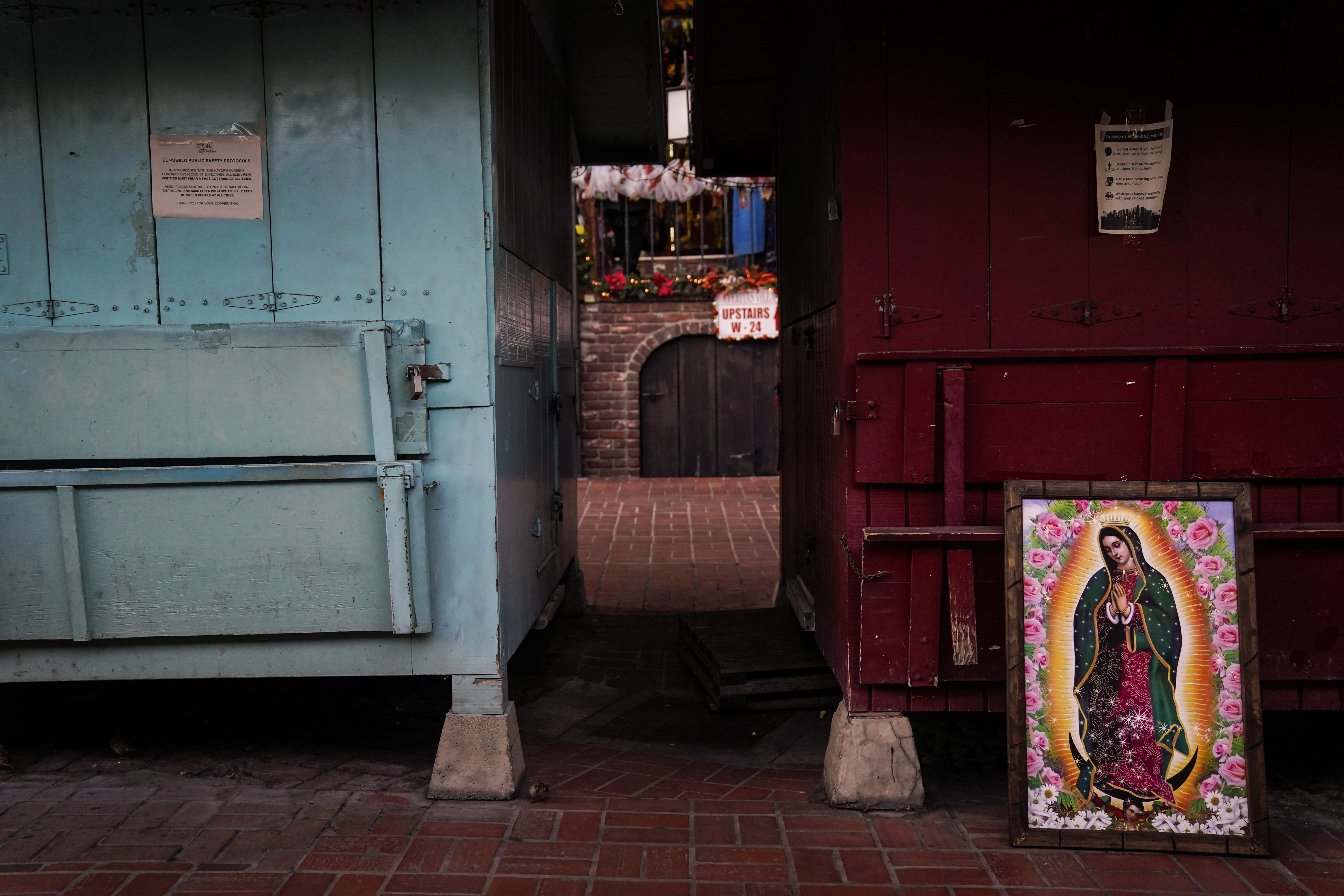 A framed painting depicting Our Lady of Guadalupe is propped against a shuttered market stall on empty Olvera Street in downtown Los Angeles, Wednesday, Dec. 16, 2020. Olvera Street, known as the birthplace of Los Angeles, has been particularly hard hit by the coronavirus pandemic, with shops and restaurants closed and others barely hanging on. (Jae C. Hong / Associated Press)