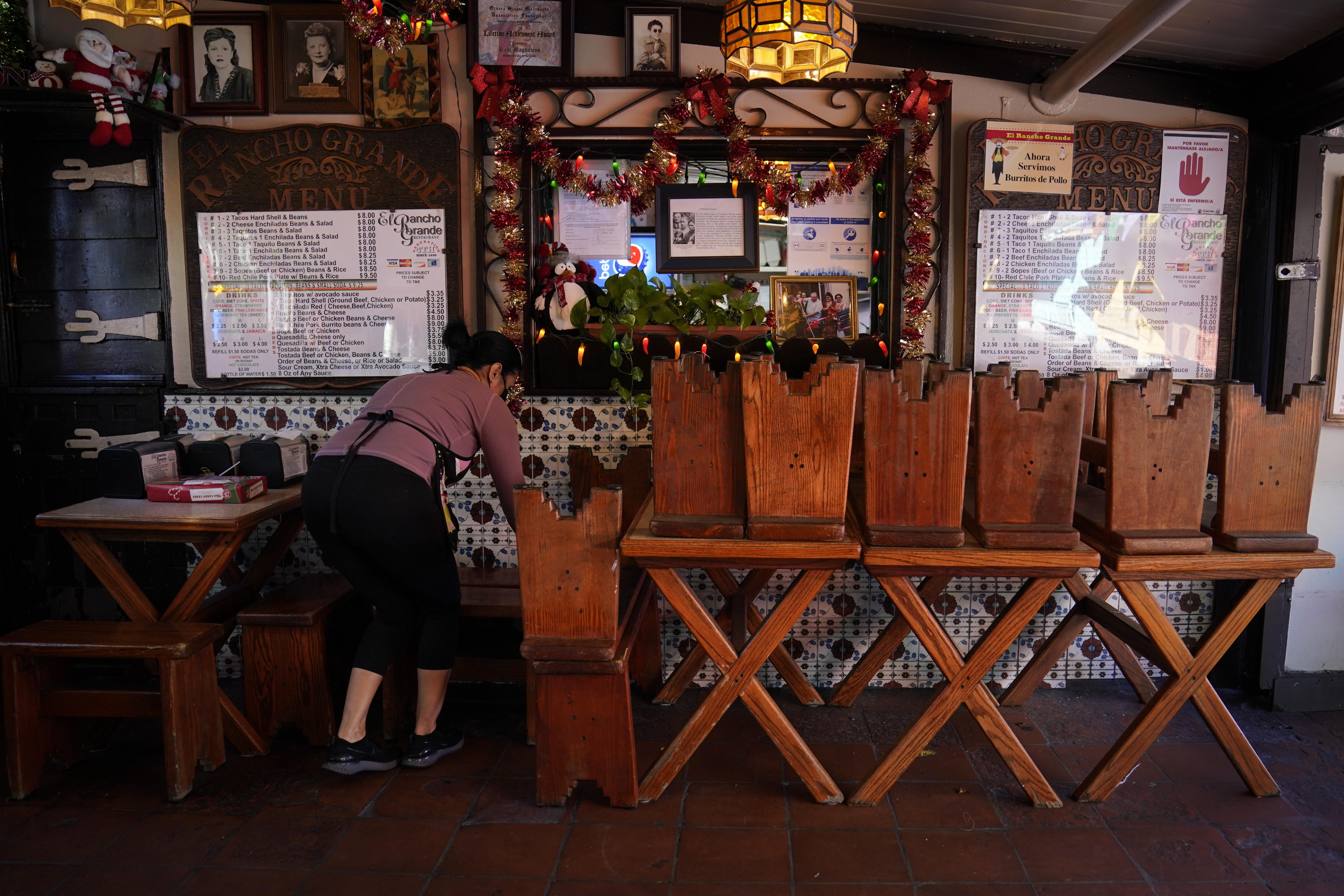 Debbie Briano, a fourth-generation owner of Mexican restaurant, El Rancho Grande, works in her restaurant next to chairs and tables pushed against the wall on Olvera Street in downtown Los Angeles, Wednesday, Dec. 16, 2020. Briano still decorated her cafe like she normally would at Christmas. She bought poinsettias, put up a real tree, hung tinsel, lights, and strung little snowmen and Santa Claus above her window. "I had to do that to feel normal," she said. "I' m not going to let COVID take away our Christmas magic." (Jae C. Hong / Associated Press)